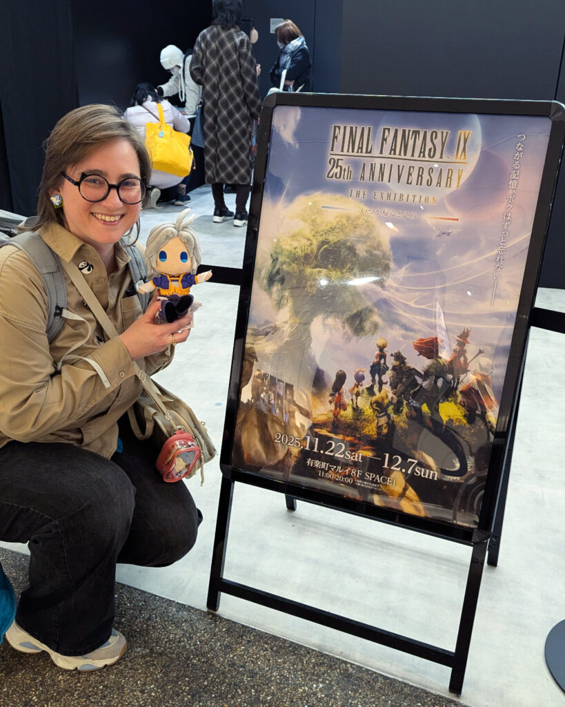 Me squatting down next to a poster advertising the FFIX exhibition. I am holding up a chibi Kuja plushie